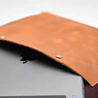 Brown leather sleeve covering a laptop with an Apple logo on a white background
