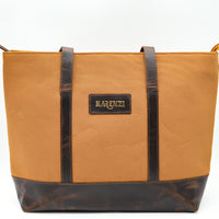 Brown tote bag with black accents and a visible brand logo on a white background