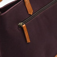 Close-up of a dark purple bag with brown leather accents on a white background