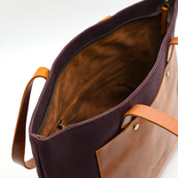 Brown leather tote bag with tan handles on a white background