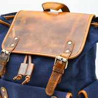 Blue backpack with brown leather straps and flap on a white background