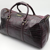 Brown leather duffel bag with crocodile texture on a white background