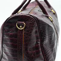 Close-up of a dark brown leather handbag with gold hardware on a light gray background