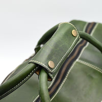 Close-up of a green leather bag with brass buttons on a white background