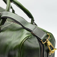 Green leather duffel bag with gold zipper and hardware on a blurred background