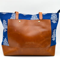 Tote bag with blue floral pattern and brown leather front on a white background