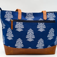 Blue tote bag with white floral pattern and brown leather accents on a white background