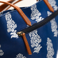 Blue bag with white floral pattern and brown leather straps on a blurred background