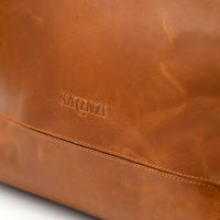 Close-up of a brown leather bag with 'KARUNI' branding on a white background