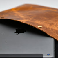 Black tablet with Apple logo inside a brown leather case on a white background