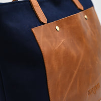Navy tote bag with brown leather accents on a white background