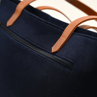 Navy blue bag with brown leather handles on a light background