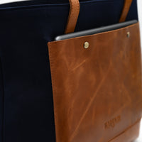 Navy blue bag with brown leather handle and patch on a white background