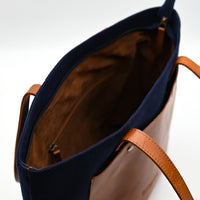 Navy blue tote bag with brown leather handles on a white background