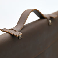Close-up of a brown leather bag with strap on a light gray background