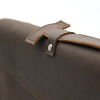 Close-up of a brown leather bag with a strap and metal buckle on a white background