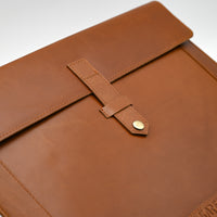 Brown leather sleeve with a flap and button closure on a white background