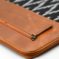 Close-up of a brown leather wallet with a zipped compartment on a patterned fabric background.