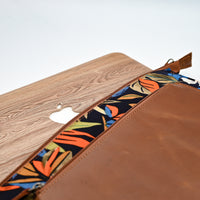 Close-up of a brown leather pouch with a colorful interior lining and wooden panel on a white background.